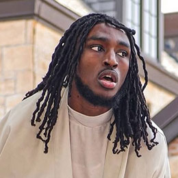 Headshot of a young Black man with long locs, looking slightly surprised.