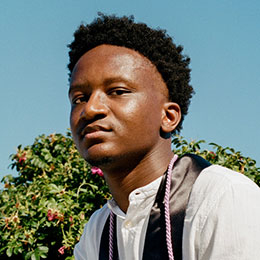 Young Black man in graduation attire poses outdoors.