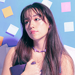 Thoughtful young woman holds a notebook against a blue background with sticky notes.