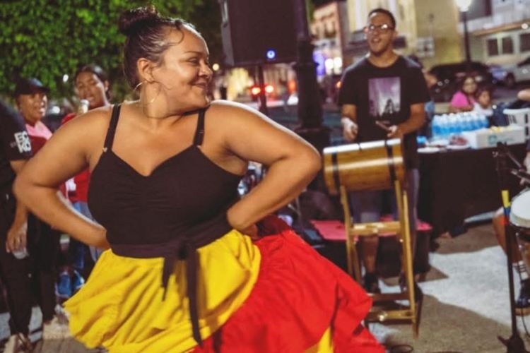 Woman in colorful dress dances to drum music at outdoor event.