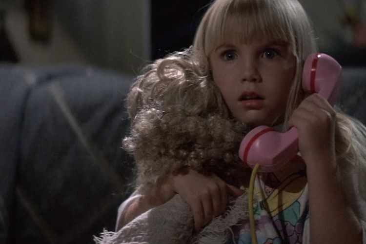 A blonde girl holding a doll and a pink phone.
