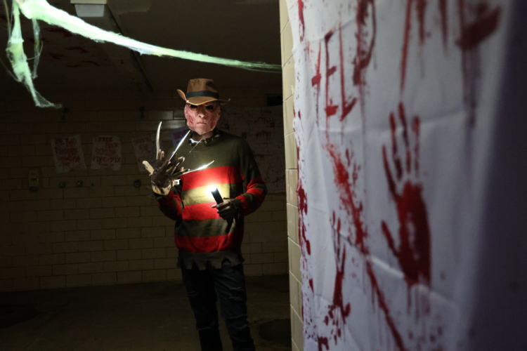 Freddy Krueger with claws and flashlight stands in haunted house.