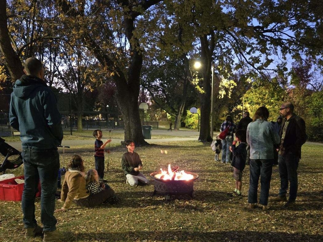 Photograph of a group of people gathered around a fire pit in a park.
