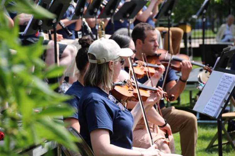 Outdoor orchestra violinists playing music on a grassy lawn.