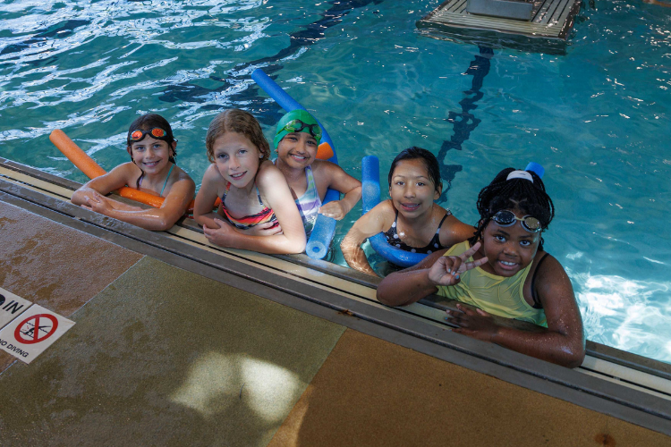 Five children in a pool with swim noodles.