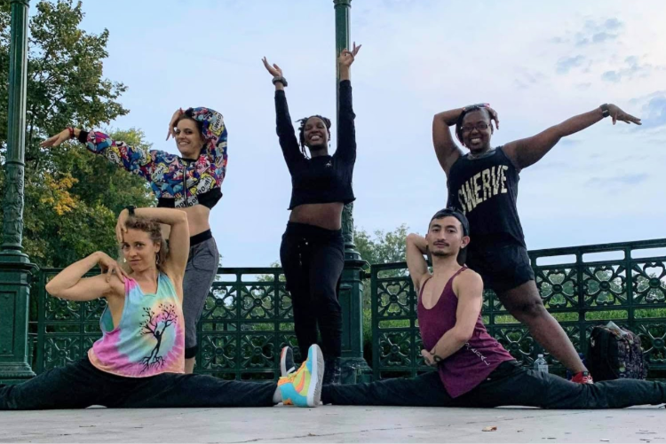 Five diverse dancers posing in a park, two performing splits.