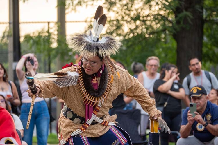 A Native American dancer in traditional regalia performing outdoors for an audience.