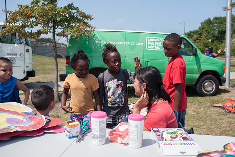 Group of children and an instructor crafting outdoors with a Chicago Park District van behind them.