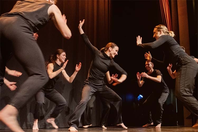 Photograph of a group of dancers in black clothing performing on a stage.