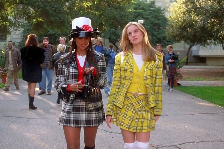 Two young women in plaid outfits walking and talking outdoors on a school campus.