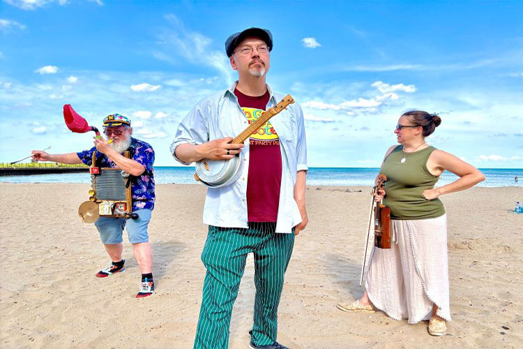Photograph of a trio of musicians playing instruments on a sunny beach.