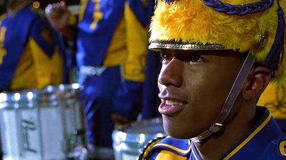 Close-up of a marching band member wearing a yellow and blue uniform and fuzzy hat.