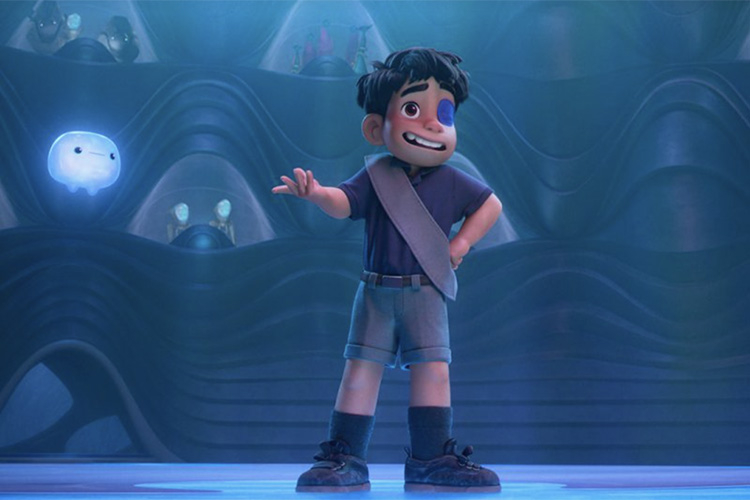 A boy with dark hair and a blue eye patch gestures while standing in a futuristic blue room.