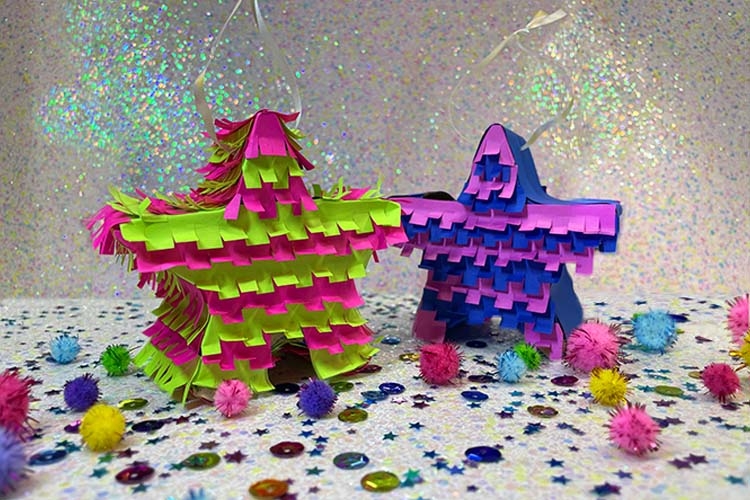 Two star-shaped piñatas, one neon green and pink and one blue and purple, on a glittery surface.