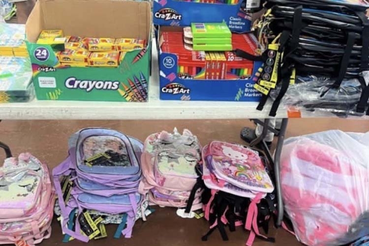 Table displaying boxes of Cra-Z-Art crayons and markers above a collection of colorful backpacks.