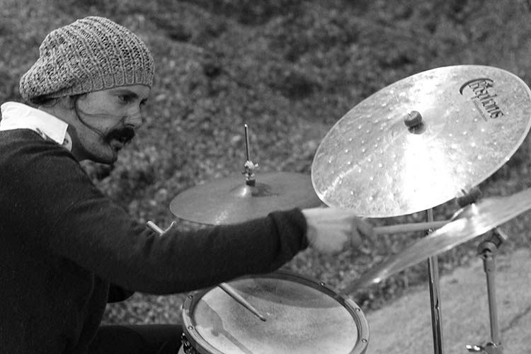 Black and white photograph of a drummer in a knit cap playing a cymbal and snare drum.