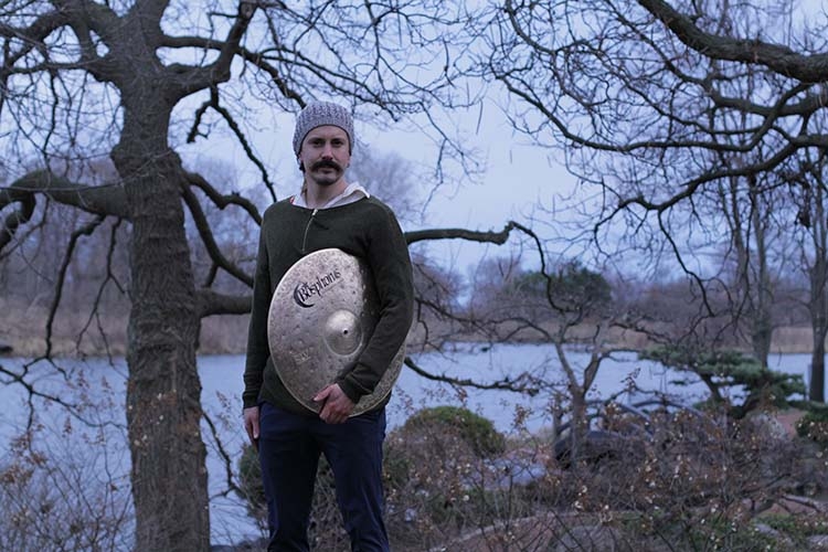 A man with a mustache and beanie holding a Bosphorus cymbal in a park.