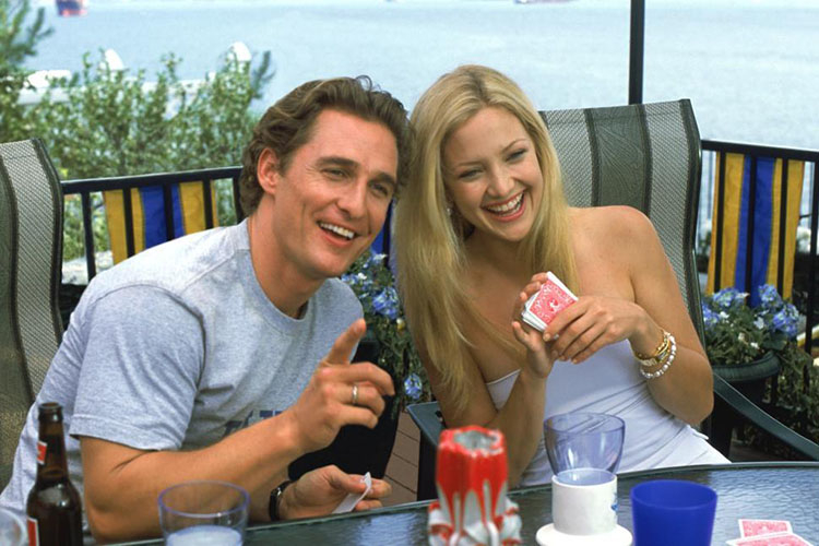 Photograph of Matthew McConaughey and Kate Hudson laughing while playing cards on a patio.