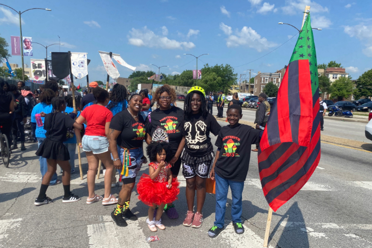 A group of people celebrating Juneteenth outdoors, holding a Pan-African flag.