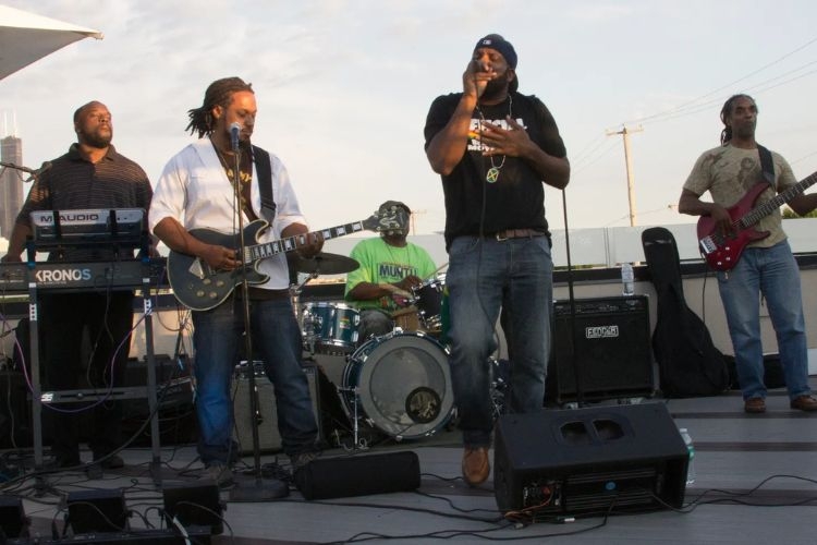 A live band performs outdoors with a vocalist, guitarist, bassist, drummer, and keyboardist.