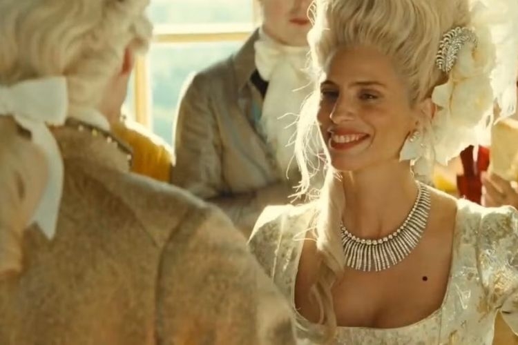 A woman in a powdered wig and period dress smiles at a man in a formal waistcoat.