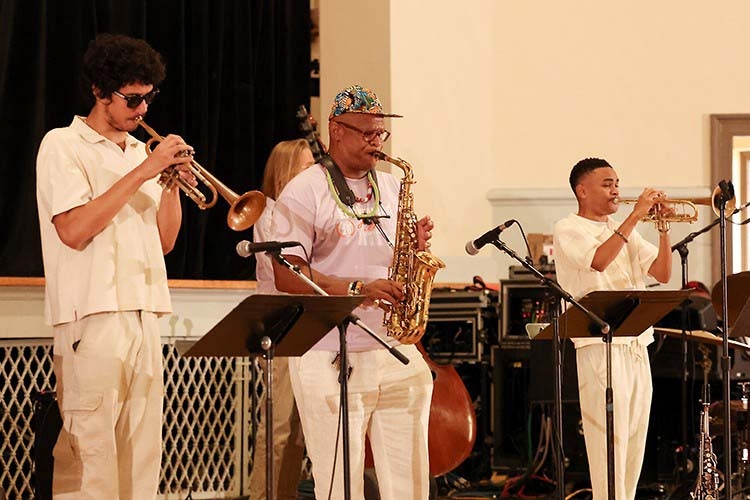 Photograph of a jazz band performing with two trumpet players and a saxophonist on stage.