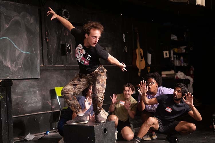 A photograph of a group of actors in a dark studio space performing with expressive poses.