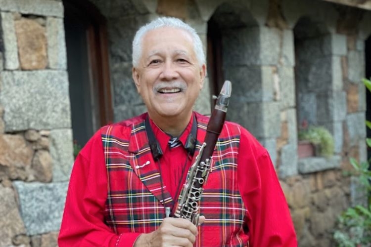 Photograph of a smiling older man wearing a red plaid vest and holding a clarinet.