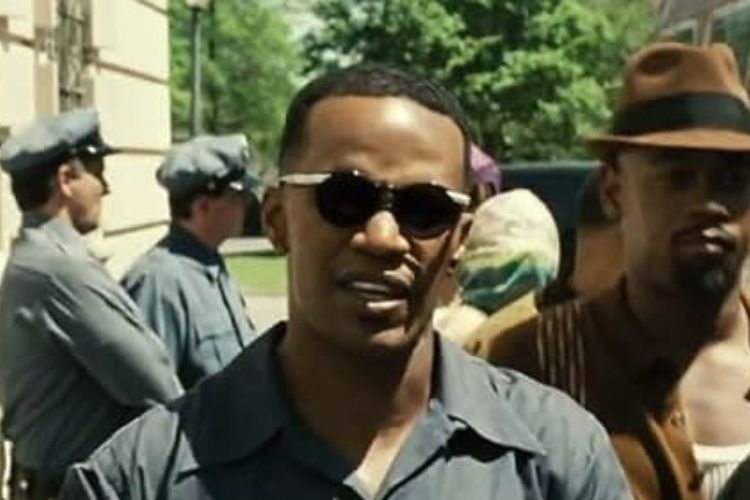 Photograph of a man in sunglasses with uniformed officers in the background.