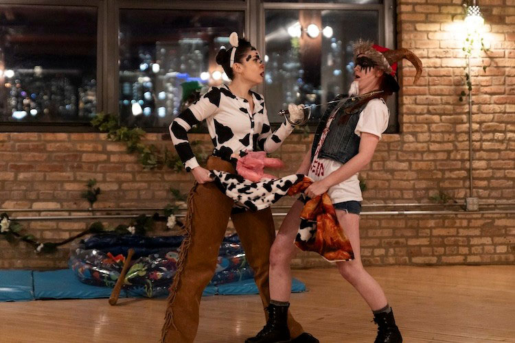 Two people in costumes staging a mock duel with a small sword in a studio with a brick wall.