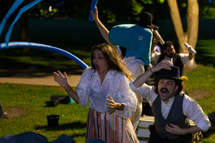 Photograph of performers in period clothing reacting dramatically outdoors at night.