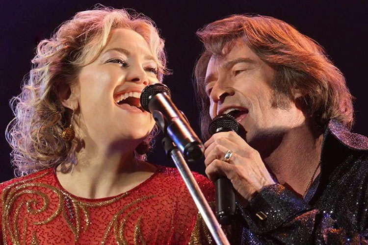 Photograph of Kate Hudson and Hugh Jackman singing into microphones on stage.