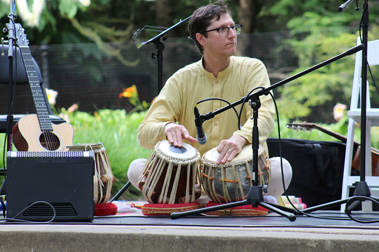 Man in a yellow shirt playing tabla drums on an outdoor stage.