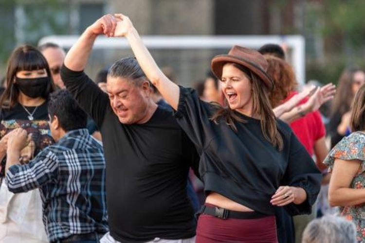 A man and woman dancing together outdoors, both smiling and looking joyful.