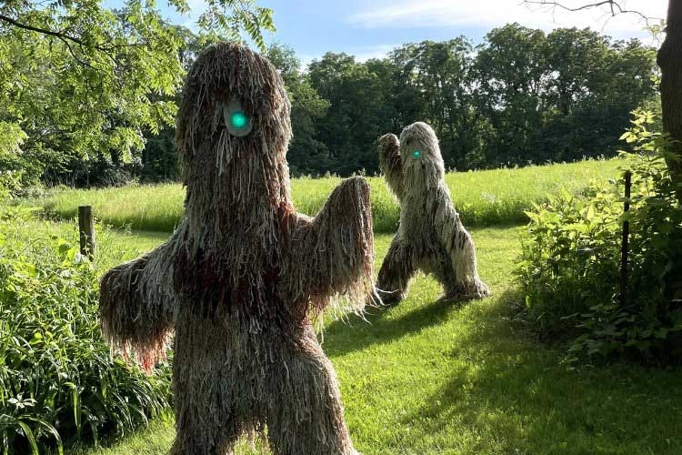 Photograph of two shaggy, humanoid creatures with glowing green eyes standing in a grassy meadow.