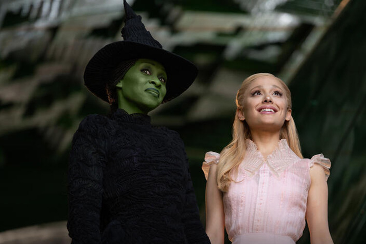A photograph of Elphaba in a black witch's hat and Glinda in a pink dress looking upward.