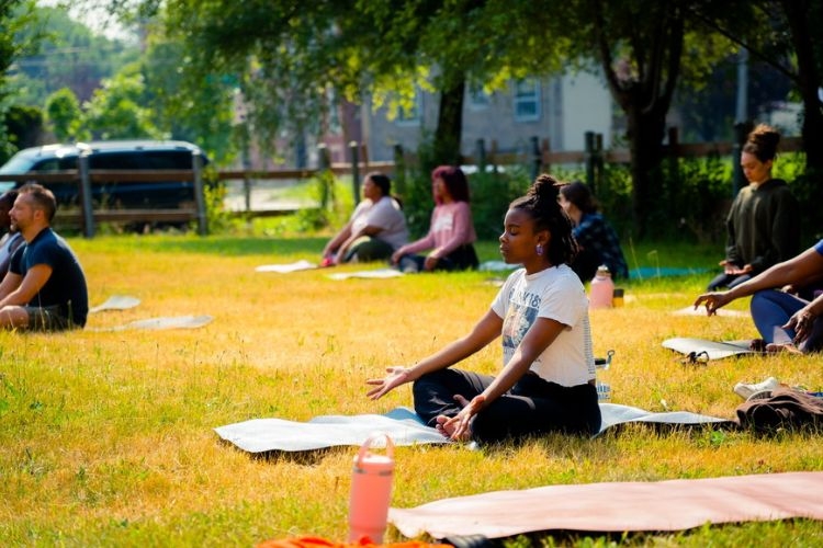 Photograph of a diverse group of people practicing yoga in a sunny outdoor field.