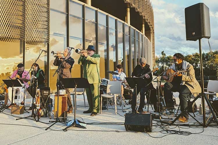 A live jazz band performs outdoors in front of a modern building at sunset.
