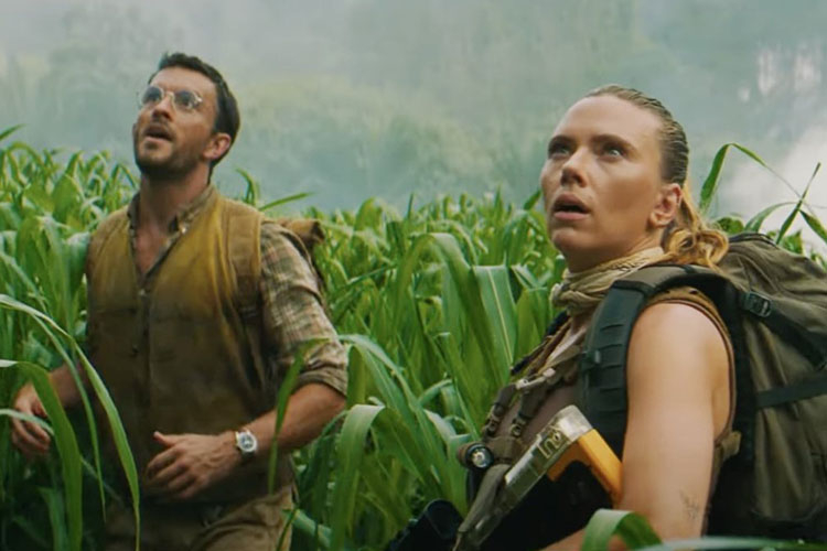 Two explorers look up in surprise while walking through a tall field of green grass.