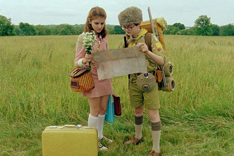 A girl and a boy in a scout uniform study a map in a grassy field.
