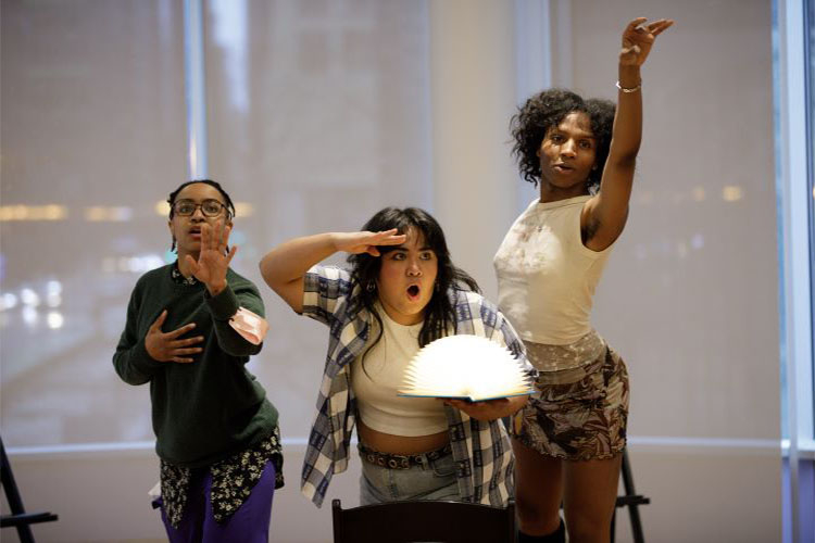 Three people striking expressive poses, one holding an illuminated circular book.