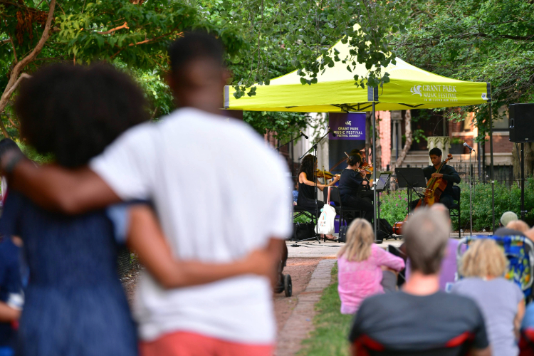 String ensemble performs under a tent for an outdoor audience in a park.