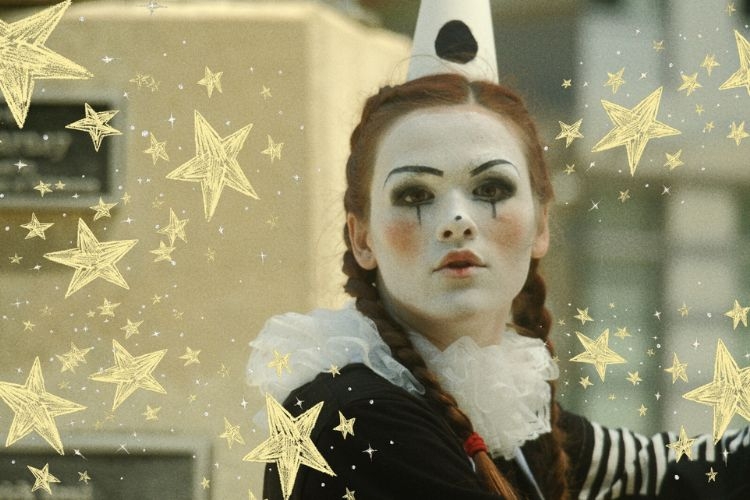 Photograph of a person in mime makeup and a party hat surrounded by yellow hand-drawn stars.