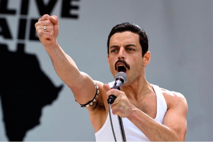 Rami Malek as Freddie Mercury singing into a microphone with his fist raised at Live Aid.