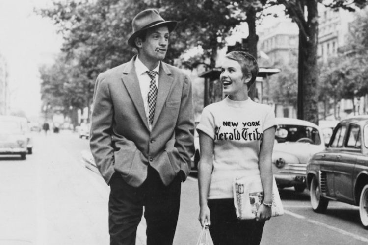 Black and white photograph of a man in a hat and a woman in a newspaper t-shirt walking on a street.