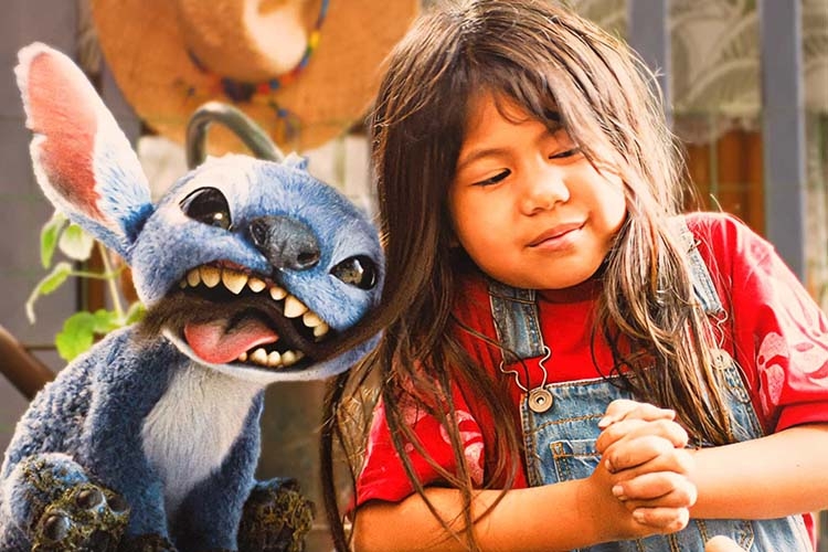 A young girl with long dark hair smiles at Stitch, the blue alien, who is biting her hair.