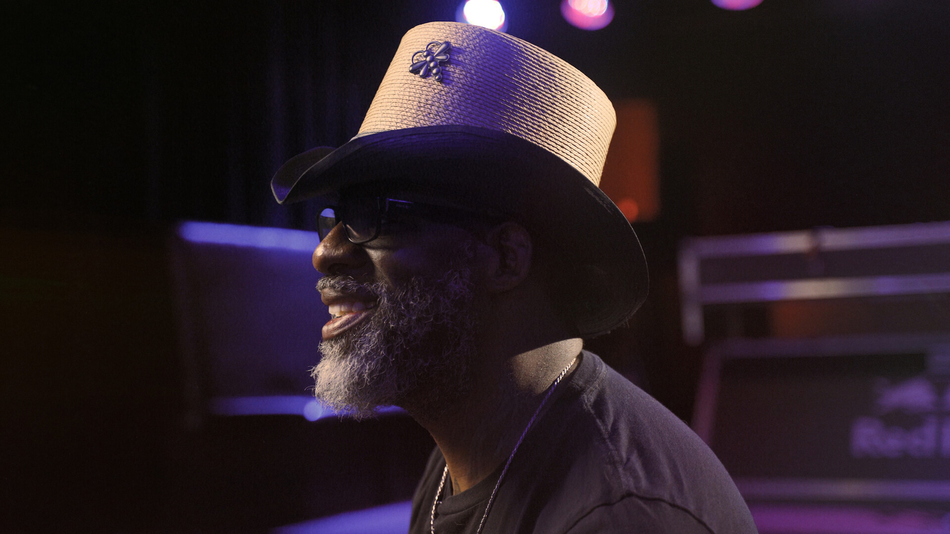 Profile photograph of a smiling man with a grey beard wearing a straw hat with a bee pin.