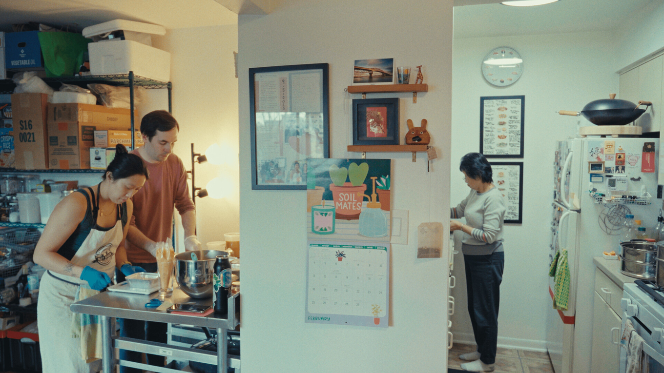 Two people bake in a kitchen while another person works in the background.