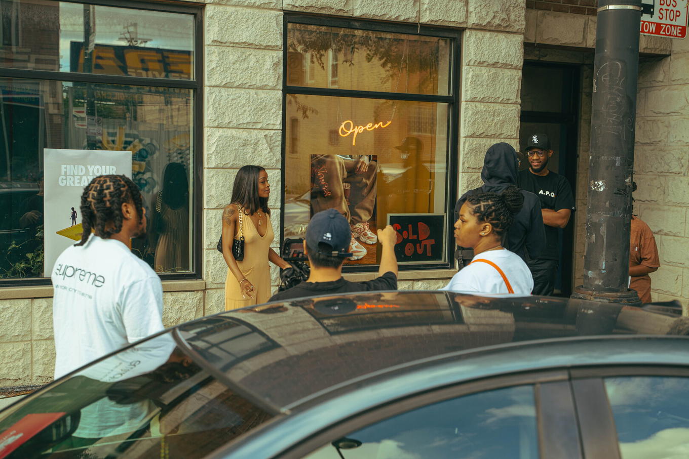 A small film crew filming a woman in a yellow dress outside a storefront window.