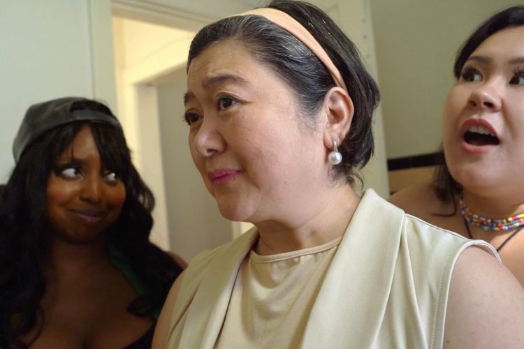 A woman in a beige top and headband looks slightly pensive, flanked by two other women.